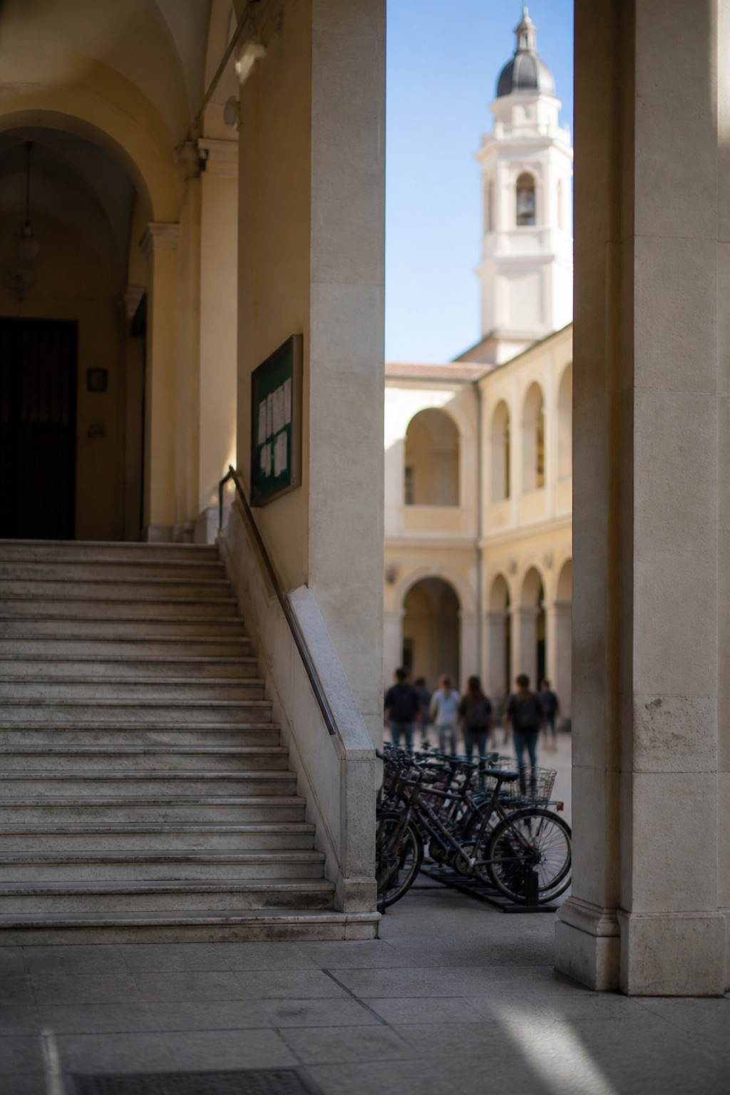 Cortile di un istituto tecnico italiano con loggiata in stile razionalista, scalinata di marmo e bacheca di avvisi sfocati